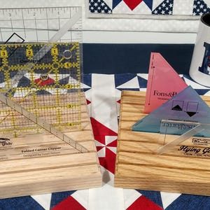 May include: A collection of quilting tools, including clear acrylic rulers and templates, displayed on wooden blocks. A mug with a blue and white design is also present. The tools are designed for precise fabric cutting and are ideal for quilting projects.