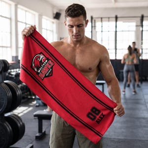 May include: A red sports towel with black stripes and the text "Waltham Hawks Hockey" and a hawk logo. The towel also features the number "08" and the name "ALEX" in black. The towel is being held in a gym setting.