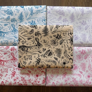 May include: A collection of fabric squares featuring various floral and rabbit patterns. The fabrics showcase designs in blue, red, pink, and purple, with a central square in beige and black. The patterns include rabbits, flowers, and ferns.