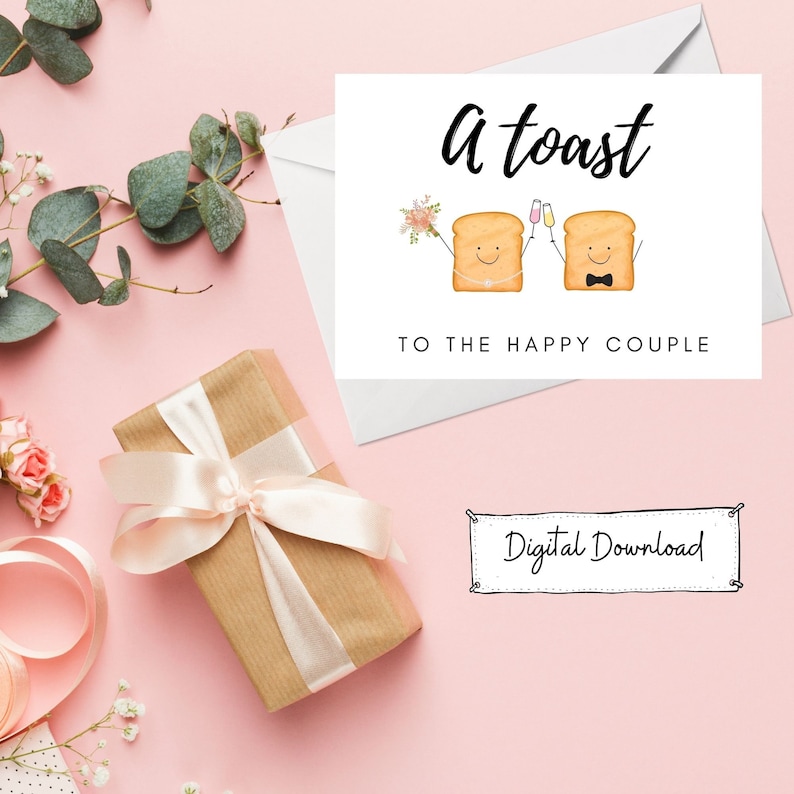 May include: A digital download card with a pink background and a white card with the text "A toast to the happy couple" and a cartoon image of two pieces of toast with faces, holding glasses of champagne. The card has a banner with the text "Digital Download".