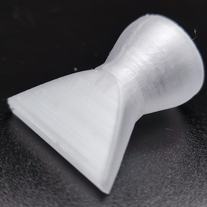 May include: A white plastic nozzle with a wide, flat opening and a narrow, round opening. The nozzle is designed to direct a stream of liquid or air.