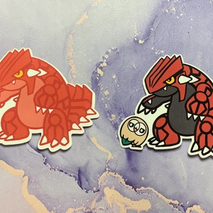 May include: Two cartoon stickers of a red and black Pokemon character with a smaller green and white Pokemon character next to it.