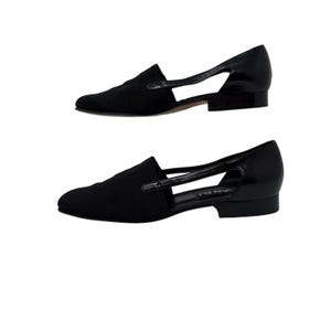 May include: Black leather and fabric slip-on shoes with a cut-out design. The shoes have a low heel and a pointed toe.