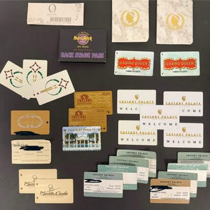 May include: A collection of various casino cards and tokens, including a Hard Rock Hotel Las Vegas backstage pass, Casino Queen cards, and Caesars Palace cards. The cards feature different designs and text, such as "Welcome" and "Come".