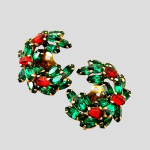 May include: A pair of crescent-shaped clip-on earrings featuring a cluster of marquise-cut emerald green crystals and round-cut ruby red crystals set in a gold-tone metal frame, arranged in a dense, layered floral or wreath-like pattern.