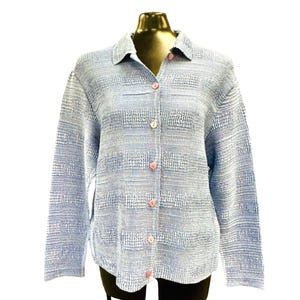 May include: A long-sleeved button-down shirt in a light blue and white textured fabric. The garment features a classic collar, a full-length front button placket with six light-colored buttons, and a horizontal striped pattern throughout the material.