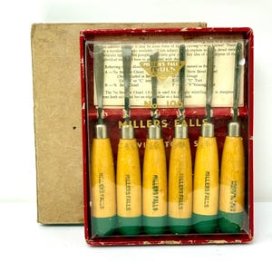 May include: A Millers Falls No. 106 carving tool set in a red box with a clear plastic cover. The set includes six metal chisels and gouges with light wood handles featuring green painted ends and the brand name printed in black ink.