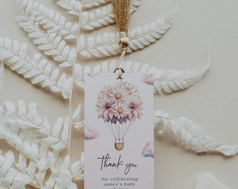 Può includere: Un'etichetta di ringraziamento bianca con un'illustrazione di una mongolfiera. Il pallone è pieno di fiori rosa e viola e galleggia sopra le nuvole. Il testo sull'etichetta dice "Grazie per aver celebrato la baby shower di Aimee."