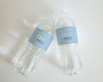 May include: Two clear plastic water bottles with light blue labels. The labels read "Sienna's ONE derful BIRTHDAY" with a daisy graphic. The bottles are filled with water and are on a white surface.