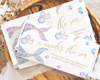 Op de afbeelding: Witte chocoladereepverpakkingen met een zeemeerminthema. De verpakkingen tonen zeemeerminstaarten, bellen en de tekst "oneder the sea" en "Thank you for celebrating Maddy's first birthday!" in gouden script.