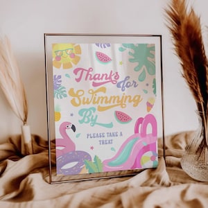 May include: A colorful sign with the text "Thanks for Swimming By. Please take a treat."  The sign features a pink flamingo, a watermelon, a blue and pink inflatable slide, a yellow sun, and a green palm tree.