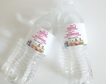 May include: Two clear plastic water bottles with white labels that say "melted snowman" in pink lettering. The labels also have a small illustration of a snowman melting into a puddle of water with a gingerbread house in the background. The text "Merry Christmas" is printed below the illustration.