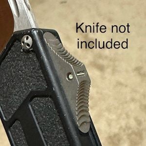Puede incluir: Primer plano de una funda de cuchillo negra y plateada con una superficie texturizada. La funda tiene un clip de metal plateado y un diseño texturizado y estriado. Cuchillo no incluido.