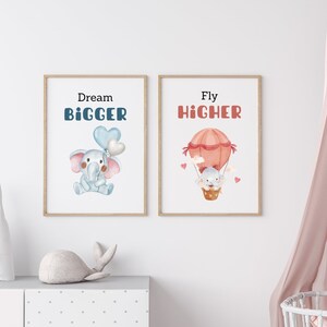 May include: Two framed prints with inspirational quotes and illustrations of elephants. The left print features a blue elephant holding balloons and the text "Dream BIGGER". The right print features a pink hot air balloon with an elephant inside and the text "Fly HIGHER".