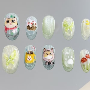 May include: Ten oval-shaped, light green nail stickers with various designs. The designs include a cat, a cupcake, a butterfly, a moon, a cup of coffee, a cat wearing a hat, a paw print, and a flower.