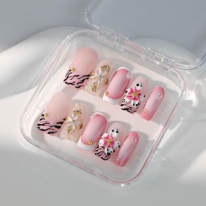Op de afbeelding: Een set roze opdruknagels met een witte punt en een zebraprint. De nagels zijn versierd met 3D-bloemen en strass.