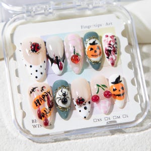 May include: A set of ten artificial fingernails with various Halloween-themed designs. The nails feature images of pumpkins, spiders, ladybugs, and cherries. Some nails have polka dots, and the text "HAPPY" is visible on one nail. The nails are in a clear plastic case.