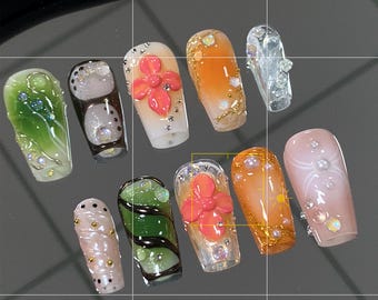 Puede incluir: Diez diseños de uñas diferentes que presentan una variedad de colores, patrones y adornos. Los diseños incluyen mármol verde, lunares marrones y blancos, una flor rosa, naranja con purpurina dorada, una uña blanca con un diseño de perla, un remolino verde, una flor rosa, naranja con purpurina dorada, una uña blanca con un diseño de perla y un remolino verde.