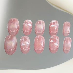 May include: Set of ten oval-shaped false nails with a pink base and white cloud designs. Some nails have a sparkly finish.