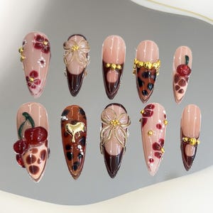 May include: Set of ten false nails with various designs. The designs include floral patterns, cherry motifs, leopard print, and gold accents.