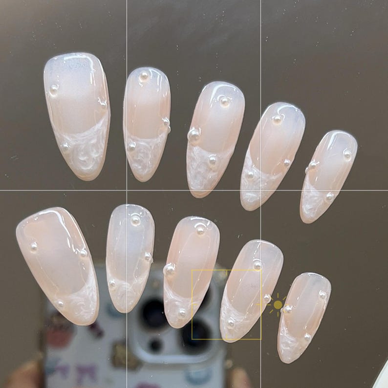 May include: Ten nude-colored fake nails with a white design and pearl accents.