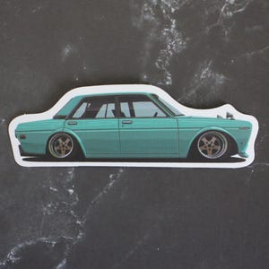 May include: A sticker featuring a teal vintage car with gold-colored rims. The car is a sedan with a white outline, set against a dark, marbled background. The car's design is low to the ground.