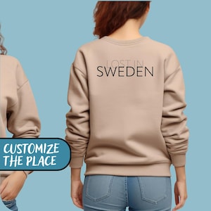 May include: A tan-colored sweatshirt with the text "LOST IN SWEDEN" printed in black on the back. The sweatshirt is a crew neck style and appears to be made of a soft material. The image shows a person wearing the sweatshirt.
