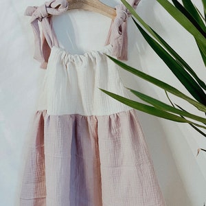 May include: A white and pink sleeveless dress with a gathered bodice and a ruffled hem. The dress is hanging on a wooden hanger with a pink ribbon tied around the straps.