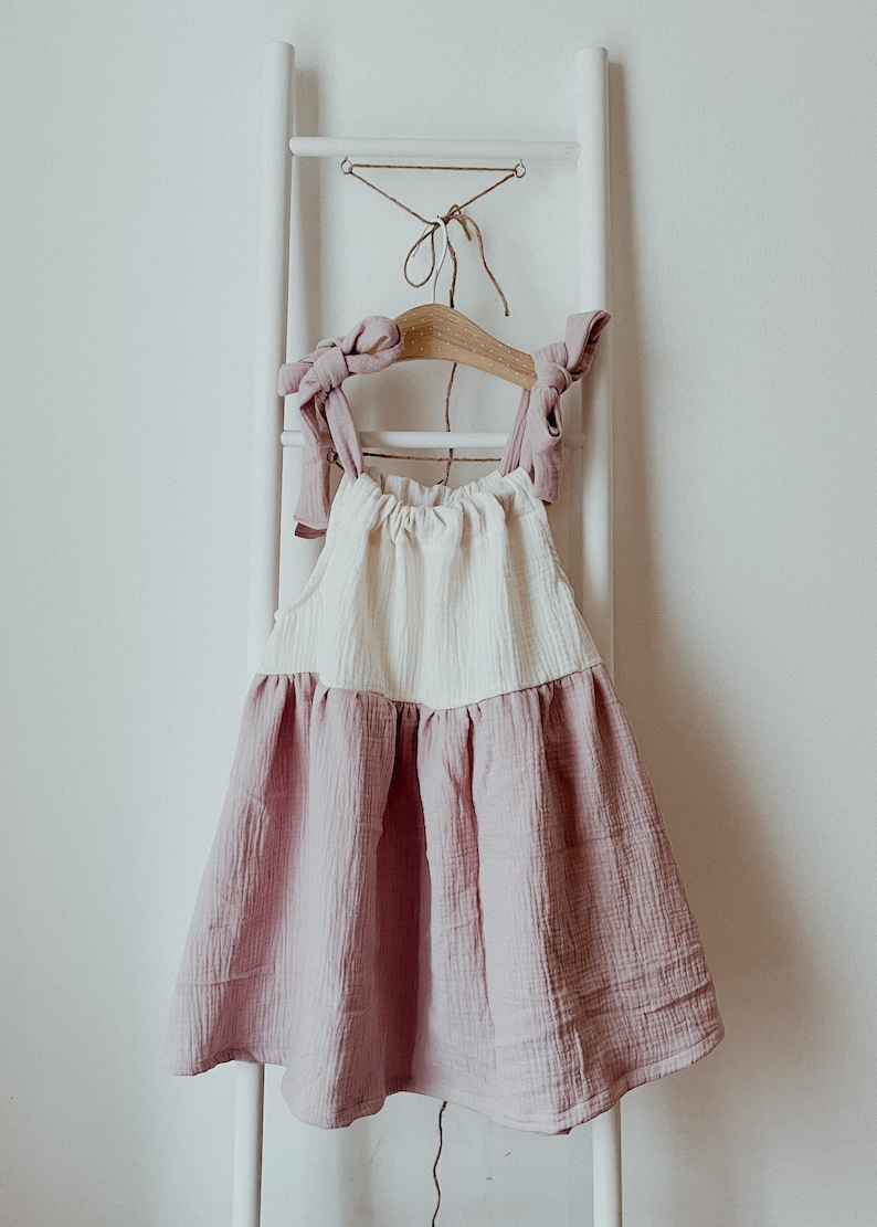 May include: A white and pink sleeveless dress with a gathered skirt and bow details on the straps.