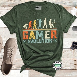 May include: Green t-shirt with the text "GAMER EVOLUTION" in orange, blue, and white. The design shows an evolution of a gamer from ape to person at a computer. A pair of gray sneakers, sunglasses, and a watch are next to the shirt.