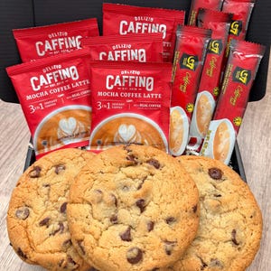 May include: Three round chocolate chip cookies arranged in front of a black box containing several red packets of Delizio Caffino Mocha Coffee Latte and G7 3-in-1 instant coffee mix. Each coffee packet features an image of a latte with heart art.
