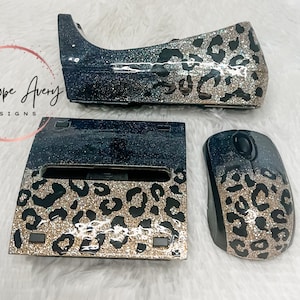 May include: A desk accessory set featuring a tape dispenser, a stapler, and a computer mouse, all finished with a black and gold glitter leopard print pattern. The items have a glossy, reflective surface and a smooth, uniform design throughout.
