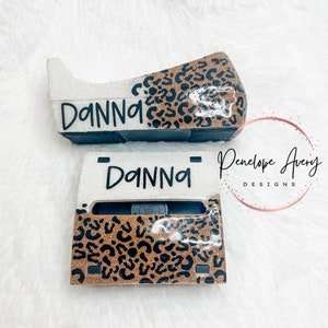 May include: A custom tape dispenser featuring a glittery silver finish on one side and a brown and black leopard print pattern on the other. The name DANNA is printed in black lettering on the silver section of the dispenser. The item is shown from two angles.