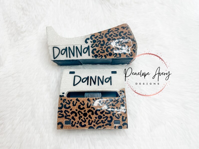 May include: A custom tape dispenser featuring a glittery silver finish on one side and a brown and black leopard print pattern on the other. The name DANNA is printed in black lettering on the silver section of the dispenser. The item is shown from two angles.