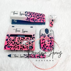 May include: A desk accessory set featuring a stapler, a tape dispenser, a computer mouse, and a pen. Each item has a white-to-pink glitter gradient finish with a black leopard print pattern and the name Toni Lynn printed in black script.