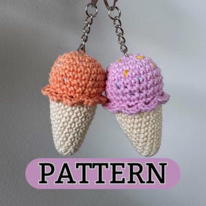 May include: Two crocheted ice cream cone keychains, one pink and one orange, with white sprinkles. The keychains are hanging from silver key rings.