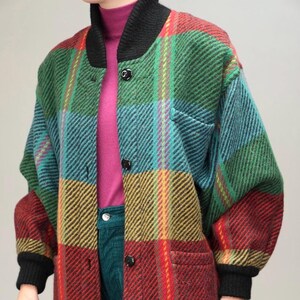 Peut inclure: Une veste en laine à carreaux surdimensionnée à manches longues avec un col et des poignets noirs. La veste est faite d'un tissu épais et tissé et présente une variété de couleurs, notamment le rouge, le vert, le bleu et le jaune.