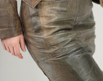 May include: A vintage brown leather jacket and matching pants. The jacket has a button closure and the pants have a fitted design. The leather appears worn, with variations in color and texture, suggesting age and use. The outfit is a classic style.