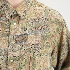 Könnte beinhalten: Langärmliges Hemd mit Patchwork-Design. Das Hemd hat eine Mischung aus beige, braunen, grünen und bordeauxfarbenen Mustern, darunter Blumen- und geometrische Motive. Es hat einen Kragen und eine Brusttasche.