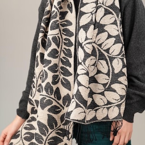 May include: A black and cream scarf with a leaf pattern. The scarf is made of a soft, woven fabric and has fringe on the ends.