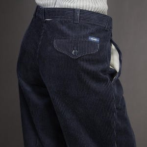 May include: Navy blue corduroy pants with a buttoned back pocket and a small label. The pants have a classic design with vertical ribbing. The fabric appears to be soft and comfortable. The pants are part of a vintage clothing collection.