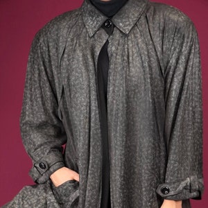 May include: A long, gray, patterned coat with a black collar and a button closure. The coat has a loose fit and a flowing silhouette.