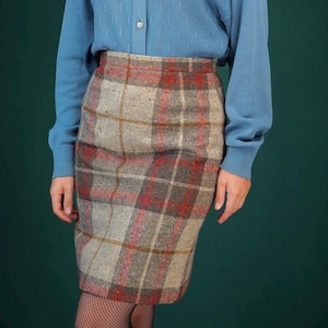 May include: A blue knitted cardigan with a button-up front, worn over a plaid skirt with brown, red, and white colours.
