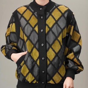 Peut inclure: Une veste bomber noire et olive avec un motif en losanges. La veste a une fermeture boutonnée et un col, des poignets et une ourlet en tricot côtelé.