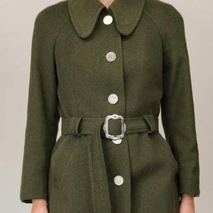 May include: A long, dark green wool coat with a large, silver buckle belt. The coat has a collar with rounded edges and a button closure.