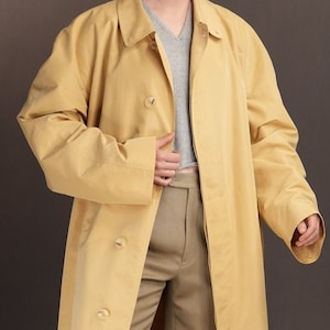 May include: A long, yellow raincoat with a button fastening and a single vent at the back. The raincoat has a classic, tailored fit and is made from a lightweight, water-resistant fabric.