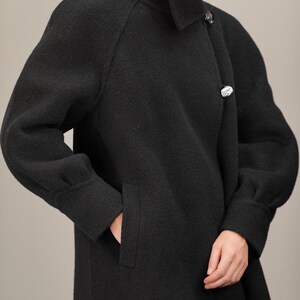 May include: A black long-sleeved coat with a high collar and a single button closure. The coat has a textured fabric and a relaxed fit.