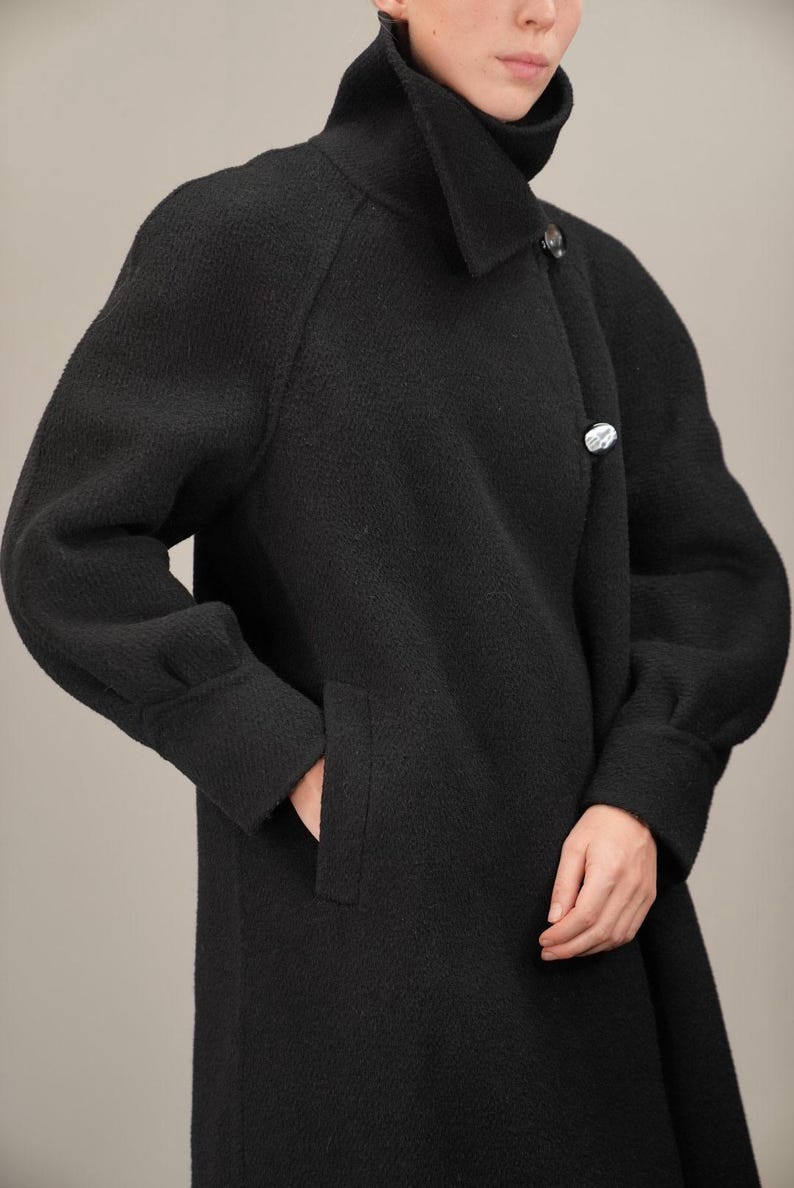May include: A black long-sleeved coat with a high collar and a single button closure. The coat has a textured fabric and a relaxed fit.