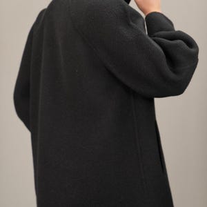 May include: A black long-sleeved coat with a high mock neck collar. The coat has a relaxed fit and a slightly gathered sleeve.