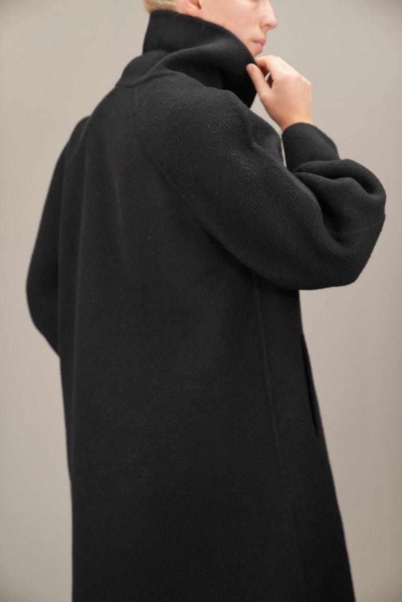 May include: A black long-sleeved coat with a high mock neck collar. The coat has a relaxed fit and a slightly gathered sleeve.